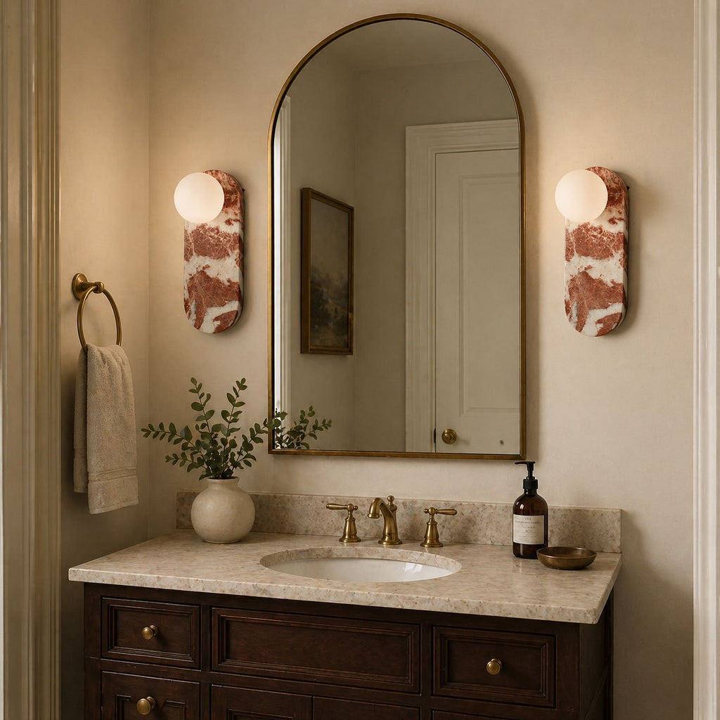 Two Clérachic sconces flank an arched mirror above a dark wood vanity, their marble bodies warmly lit in a bathroom.