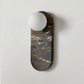 Product close-up of the Clérachic sconce in black marble with gold veining, its glass shade unlit on a plain wall.