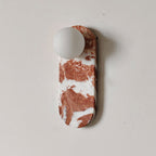 Product view of the Clérachic sconce in deep red marble with fine veining, glass shade unlit on a plain wall.