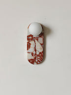 Studio shot of the red-and-white marble Clérachic sconce on a pure white background, glass shade unlit.