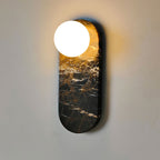 Angled view of the black marble Clérachic sconce lit warmly, its glow spreading across the wall in gold tones.