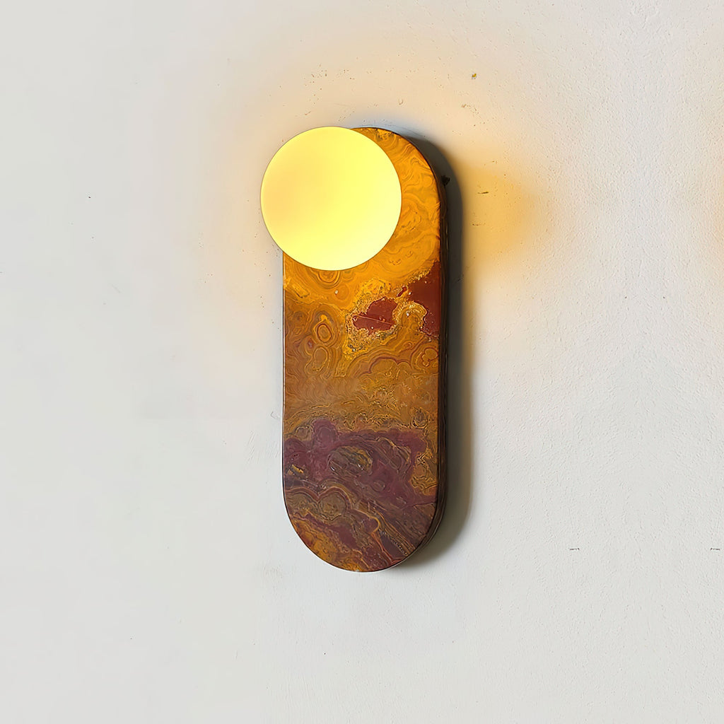 Close-up of an amber-swirled marble Clérachic sconce, its glass globe lit brightly against a plain wall.