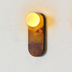Close-up of an amber-swirled marble Clérachic sconce, its glass globe lit brightly against a plain wall.