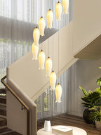 Close view of the ceramic shades lit beside a staircase, sheer curtains and a potted palm behind