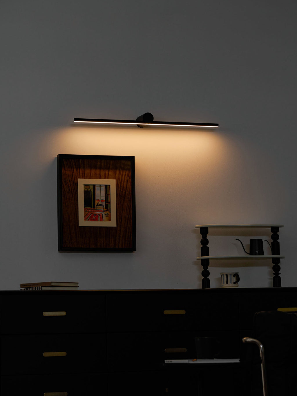 This Clérachic wall light casts a warm glow above a framed print in a moody, dark-toned bedroom.