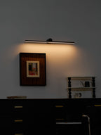 This Clérachic wall light casts a warm glow above a framed print in a moody, dark-toned bedroom.