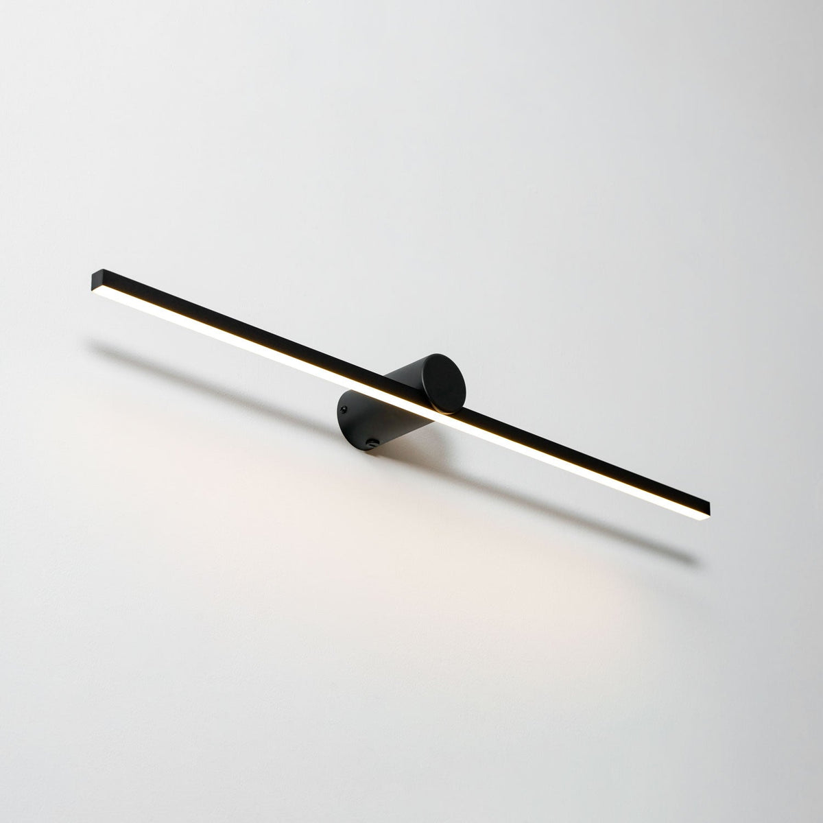 Angled studio shot of a lit Clérachic wall light, warm light spilling down a plain backdrop.