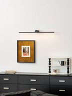 A Clérachic wall light hangs unlit above a framed print and dresser, an armchair edging into view.