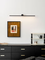 This Clérachic wall light glows warm above a framed print and dresser topped with books.