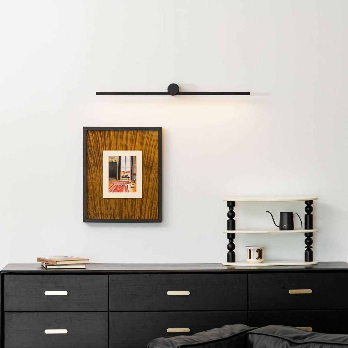 A Clérachic wall light sits unlit above a framed print, dresser, and ladder shelf with a kettle.