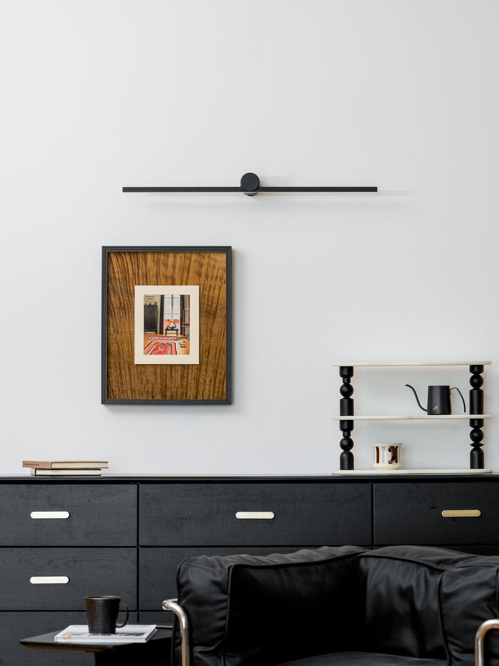 A Clérachic wall light sits unlit above a framed print, dresser, and black armchair.