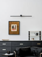 A Clérachic wall light sits unlit above a framed print, dresser, and black armchair.