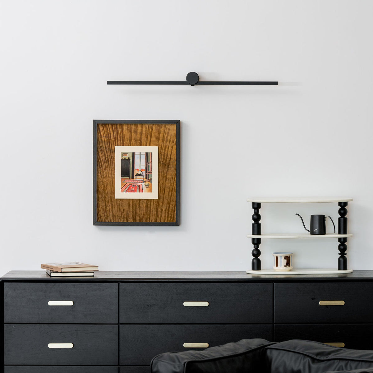 A Clérachic wall light sits unlit above a framed print, black dresser, and ladder shelf holding a kettle.