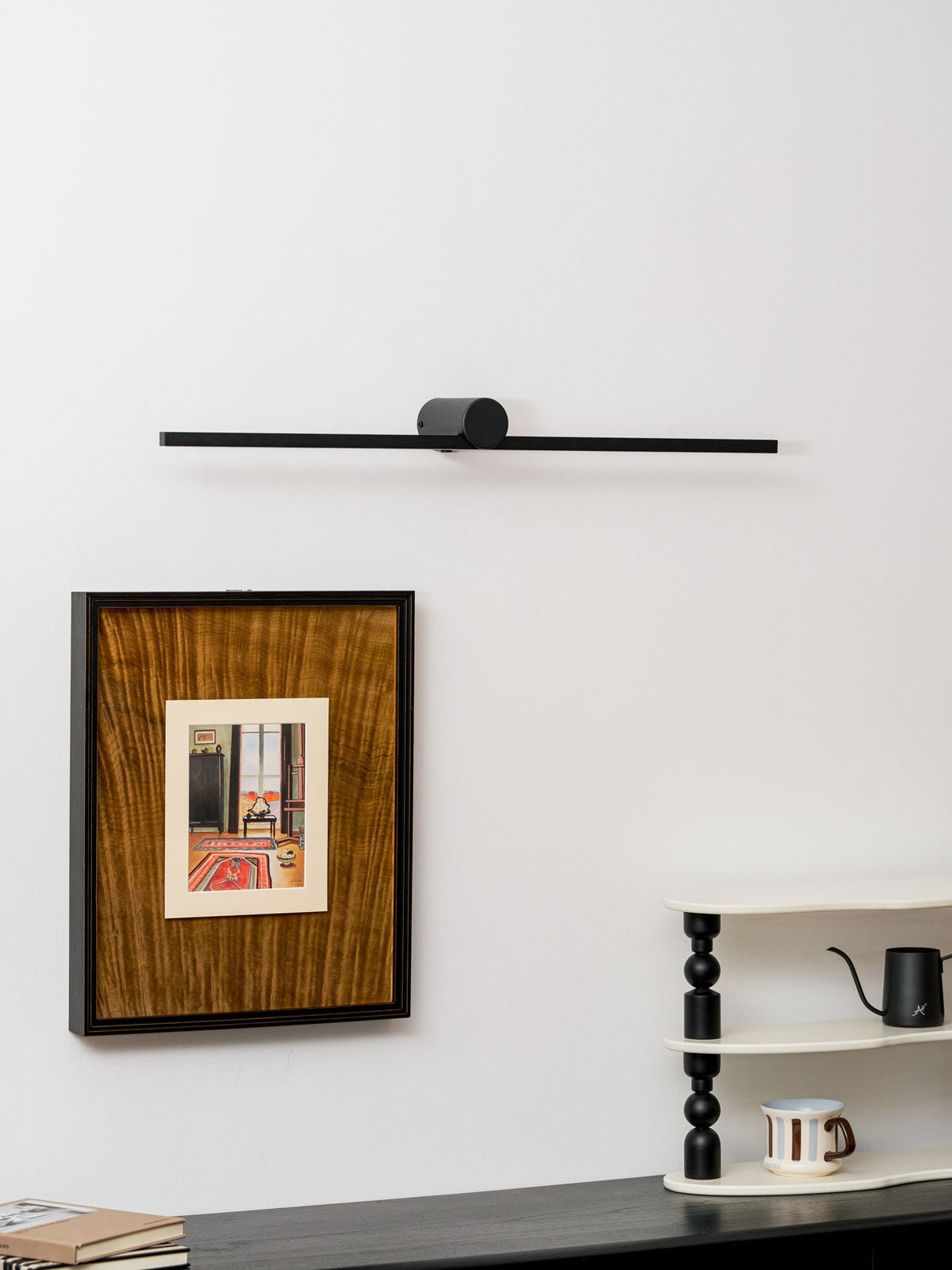 A Clérachic wall light hangs unlit above a framed print, dresser, and ladder shelf with a kettle.