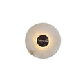 Close-up of a Clérachic alabaster wall light with a reddish-black marbled centre disc, its edge softly backlit.