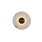 Close-up of a Clérachic alabaster wall light with a reddish-black marbled centre disc, its edge softly backlit.