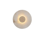 Close-up of a Clérachic alabaster wall light with a warm beige marble centre disc, its rim glowing against the pale stone.