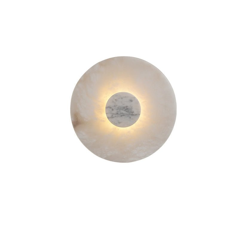 A soft warm halo rings the pale grey marble centre disc of this Clérachic alabaster wall light.