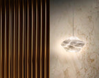 Wide view of the lit Tyler pendant on a marble wall, casting a warm halo next to amber fluted wall slats.