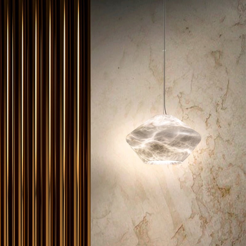 Tyler pendant lit against a beige marble wall beside fluted gold panelling, its stone shade glowing from within.