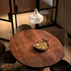 Overhead crop of the Tyler pendant lit above a round copper dining table set with a brass bowl of nuts.