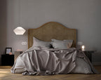 Tyler pendant hanging low beside a bed with an arched tan headboard, lit softly in a calm grey bedroom.