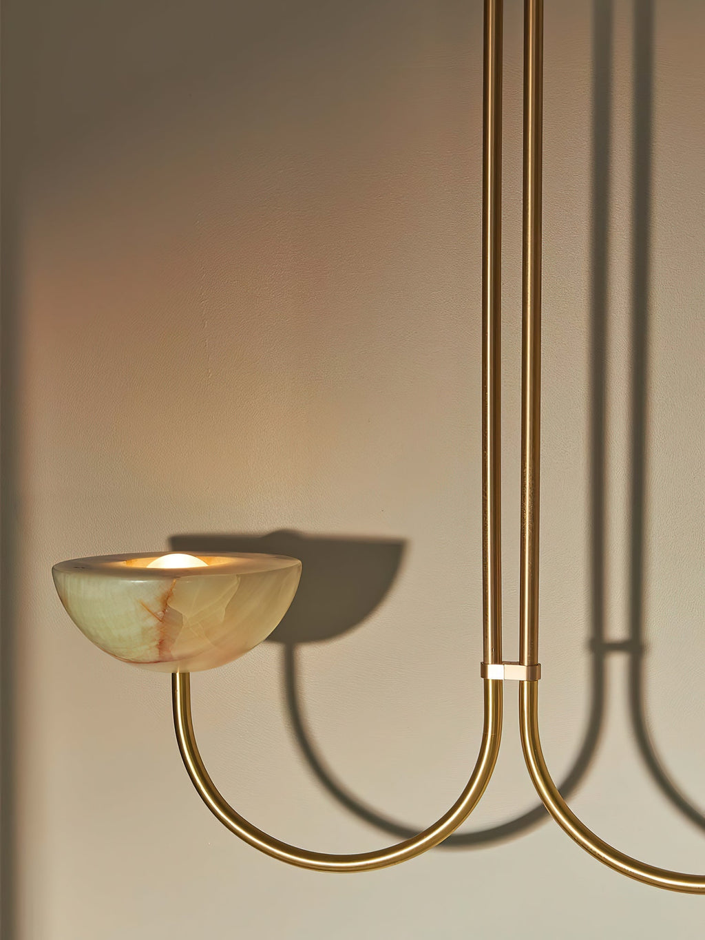 Clérachic close view of a lit jade bowl on the brass arm, the fixture's curve casting a shadow on the wall.