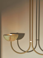 Clérachic close view of a lit jade bowl on the brass arm, the fixture's curve casting a shadow on the wall.