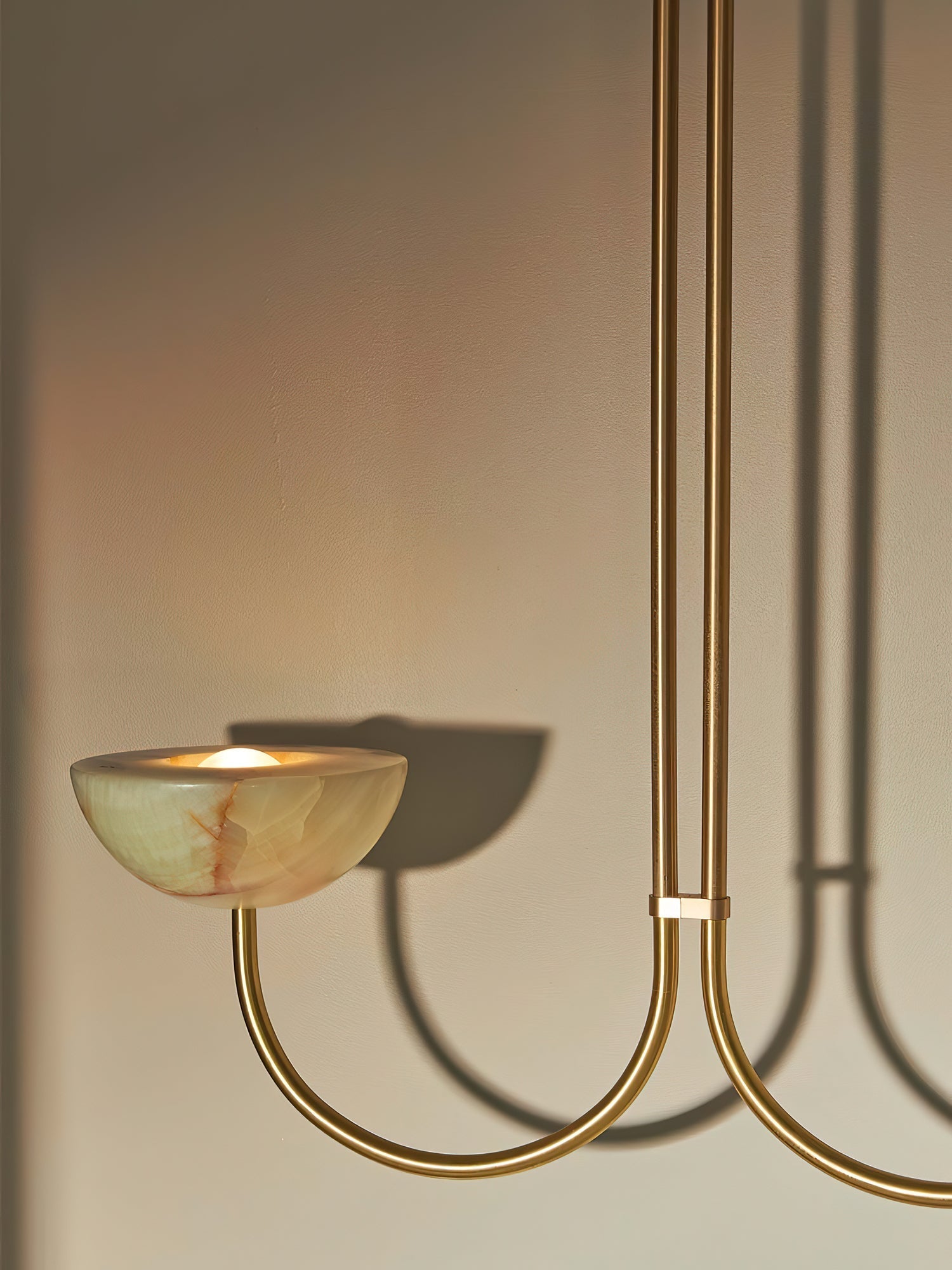 Clérachic close view of a lit jade bowl on the brass arm, the fixture's curve casting a shadow on the wall.