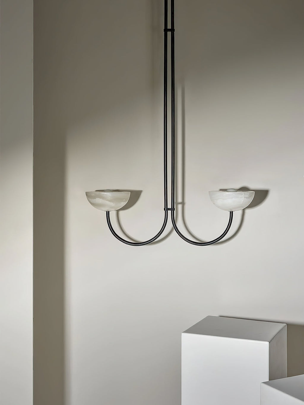 Clérachic black Lunaris pendant with alabaster bowls, its twin arms throwing soft shadows across the plaster wall.