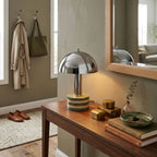 Clérachic lamp lit on an entryway console table, coat hooks and a mirror above it, shoes resting on the floor nearby.