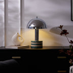 Another crop of the lit Clérachic lamp on the dark cabinet, the vase and paperback set close to its marble base.
