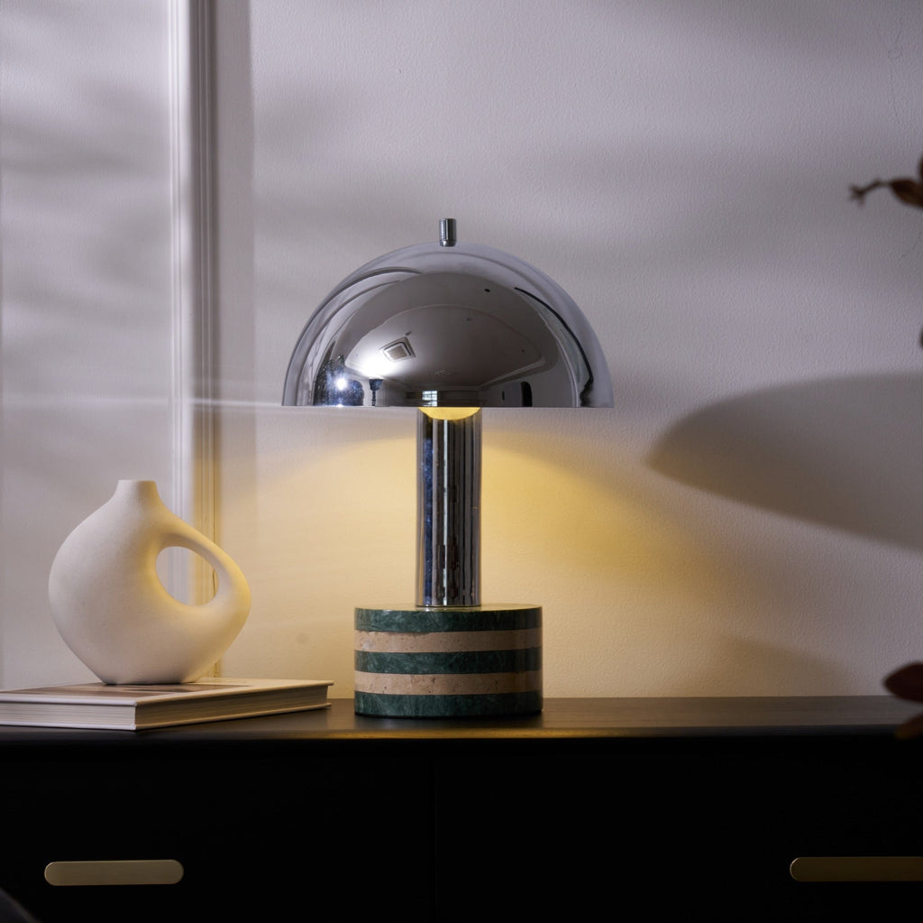 Wider view of the Clérachic table lamp lit on the dark cabinet, the ceramic vase and stacked books beside its marble base.