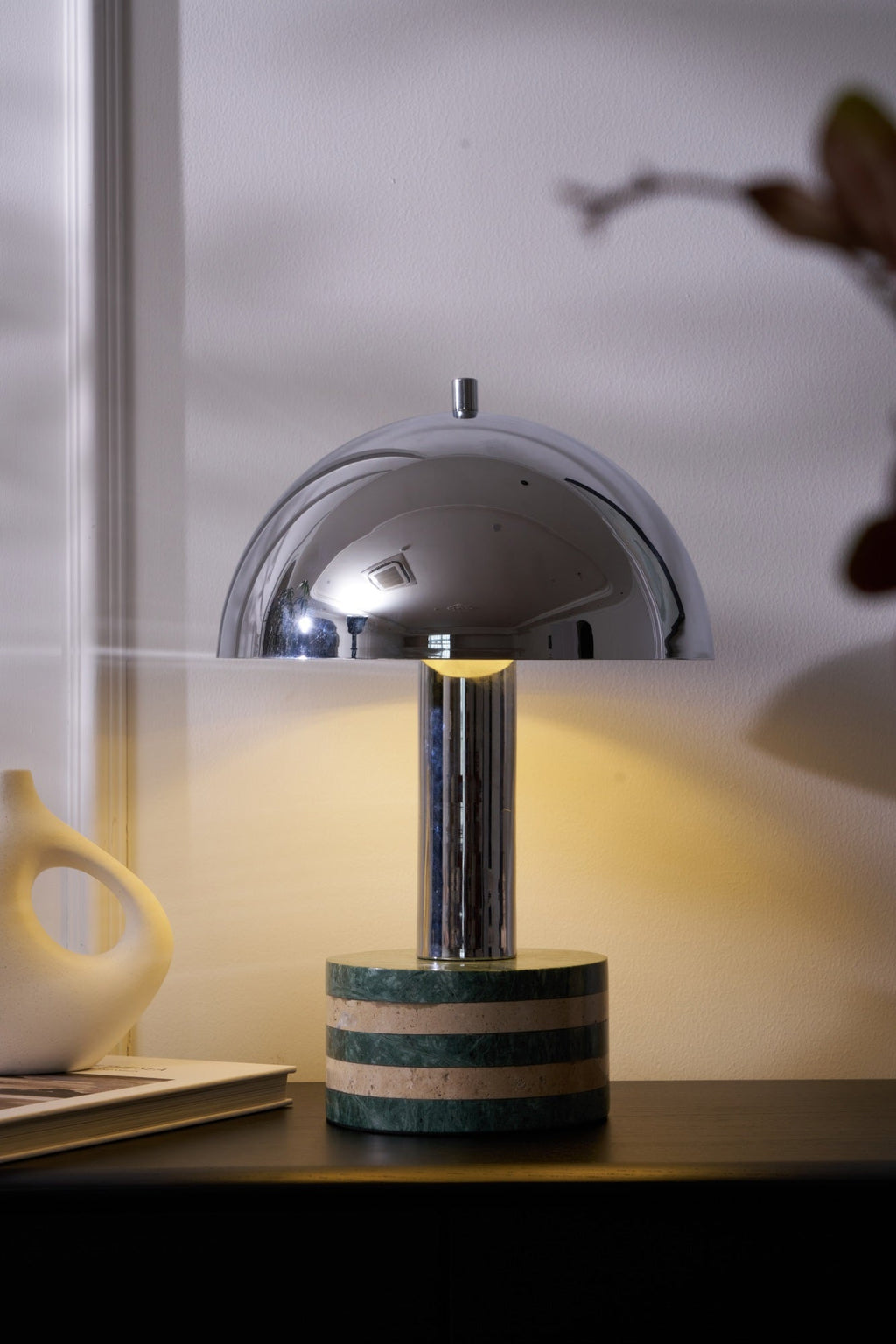 Tight crop on the Clérachic lamp's dome and marble base alone, warm light glowing against the curtained window behind.
