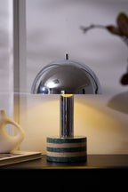 Tight crop on the Clérachic lamp's dome and marble base alone, warm light glowing against the curtained window behind.
