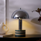 Medium crop of the lit Clérachic lamp with the vase and books to its left, warm light spilling across the cabinet top.