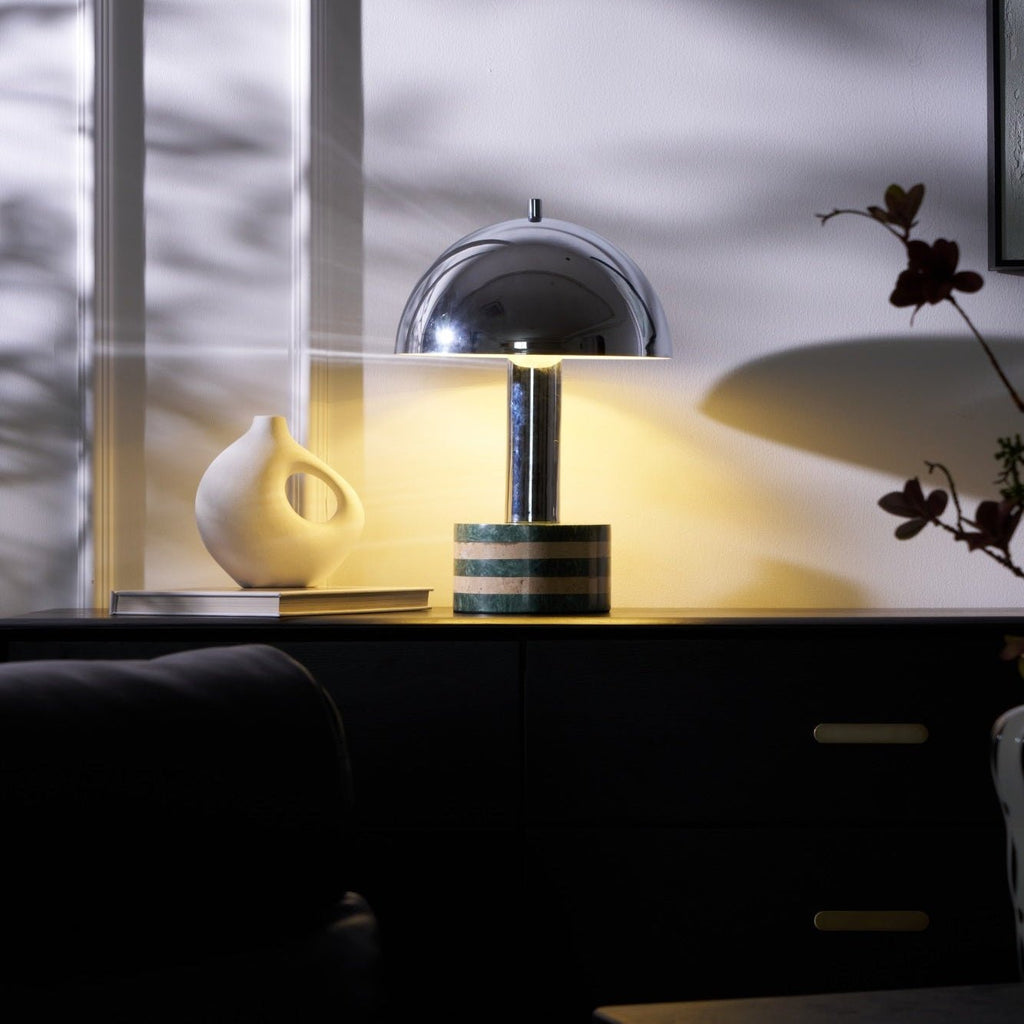 Wide shot of the lit Clérachic lamp on the cabinet, curtain shadows crossing the wall above the vase and books.