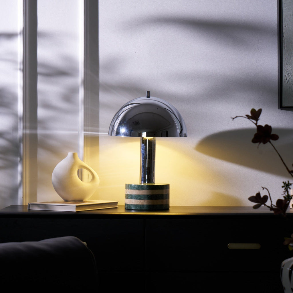 Clérachic lamp lit with its dome rim glowing, a dark branch arching into frame beside the vase and open book.