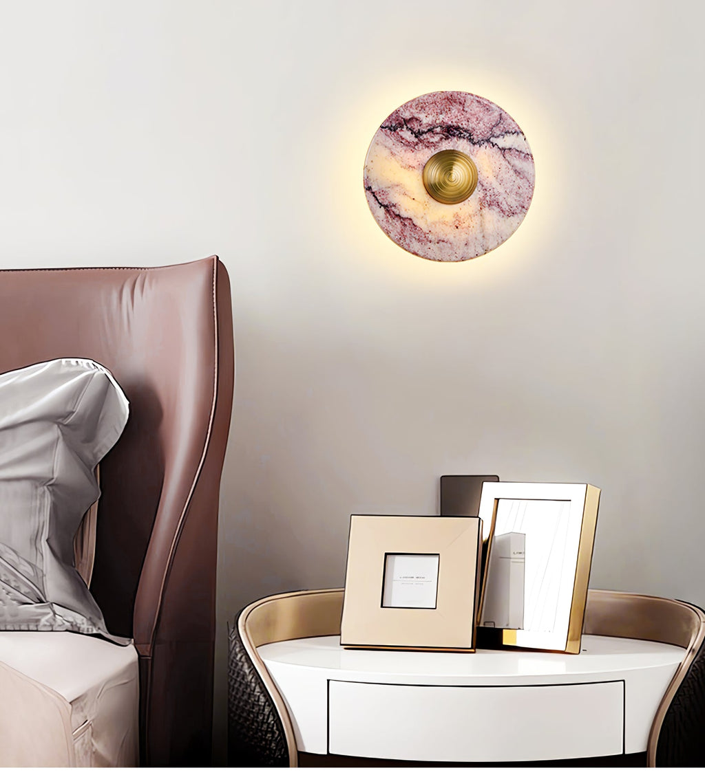 A lit Clérachic purple marble wall light hangs above a brown leather headboard, beside a round nightstand and framed photos.