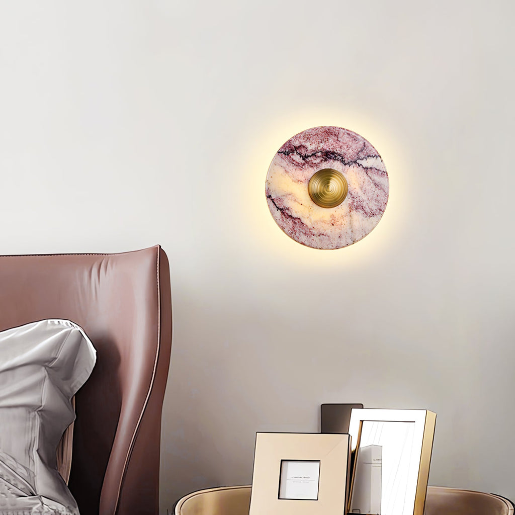A lit Clérachic wall light glows above a brown leather headboard, beside a bedside table with two framed photo frames.