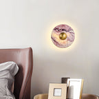 A lit Clérachic wall light glows above a brown leather headboard, beside a bedside table with two framed photo frames.