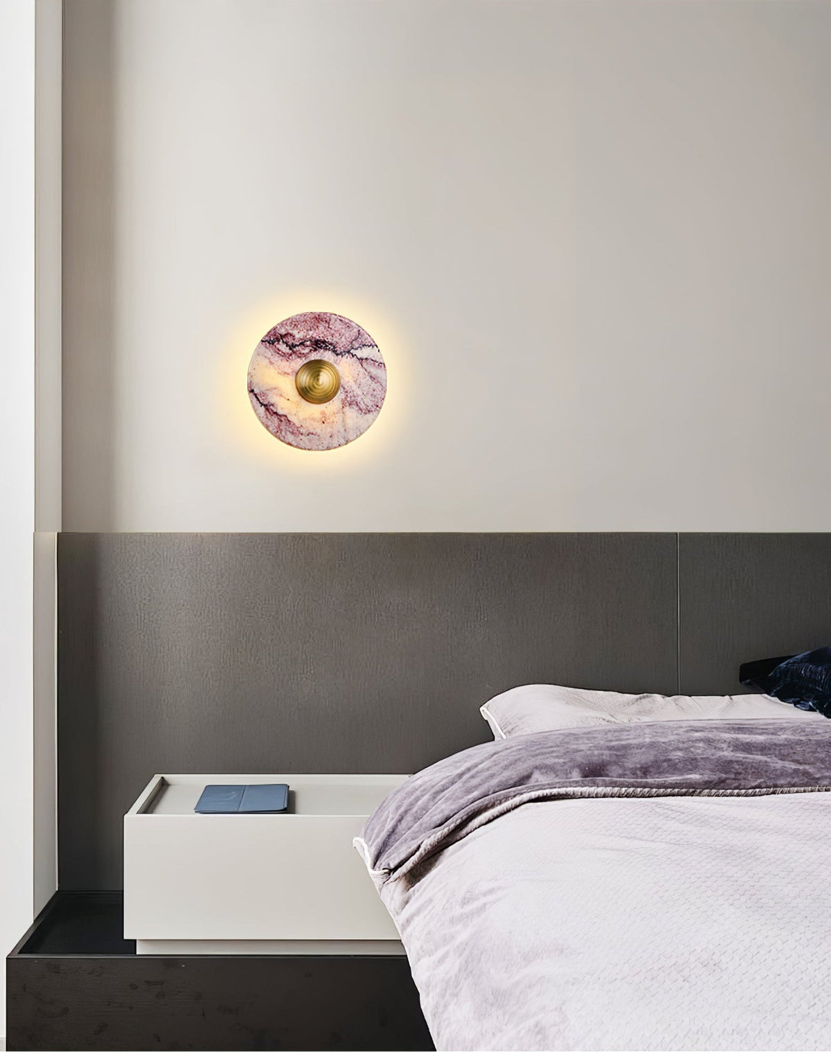 A lit Clérachic purple marble wall light glows above a charcoal headboard, beside a nightstand with a folded throw blanket.