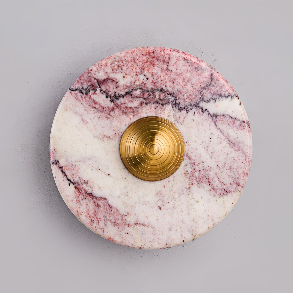 Close-up of a Clérachic wall light in purple-veined marble with a brushed gold centre knob, shown against a plain grey backdrop.