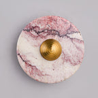 Close-up of a Clérachic wall light in purple-veined marble with a brushed gold centre knob, shown against a plain grey backdrop.