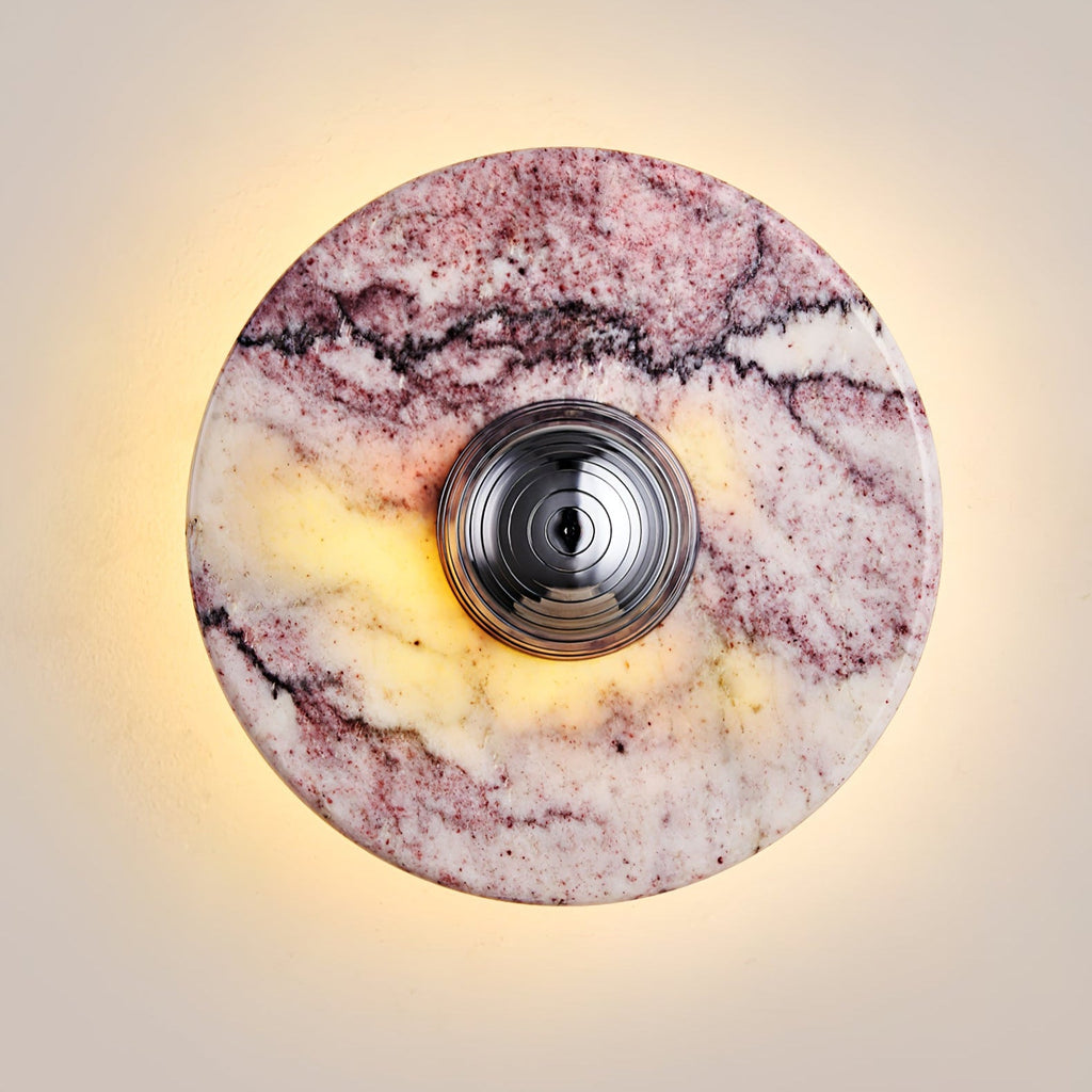 Close-up of a Clérachic wall light in purple marble with a dark gunmetal centre knob, its rim glowing with a warm backlit halo.