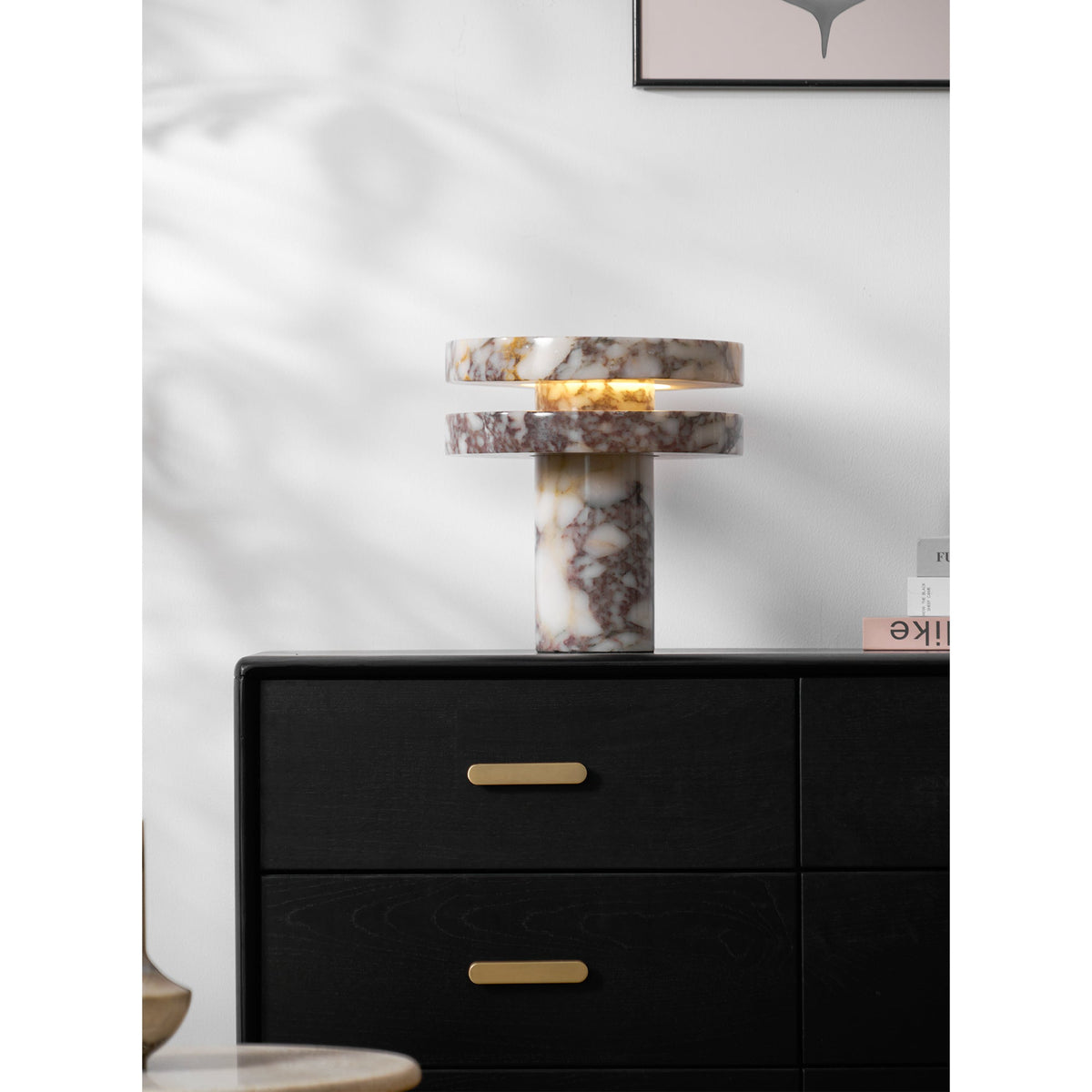 Tall crop of the lit Clérachic lamp on the dresser, its warm glow the brightest point against the plain wall.