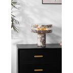 Clérachic lamp lit on the dresser with a branch reaching in from the right, books stacked just behind its base.
