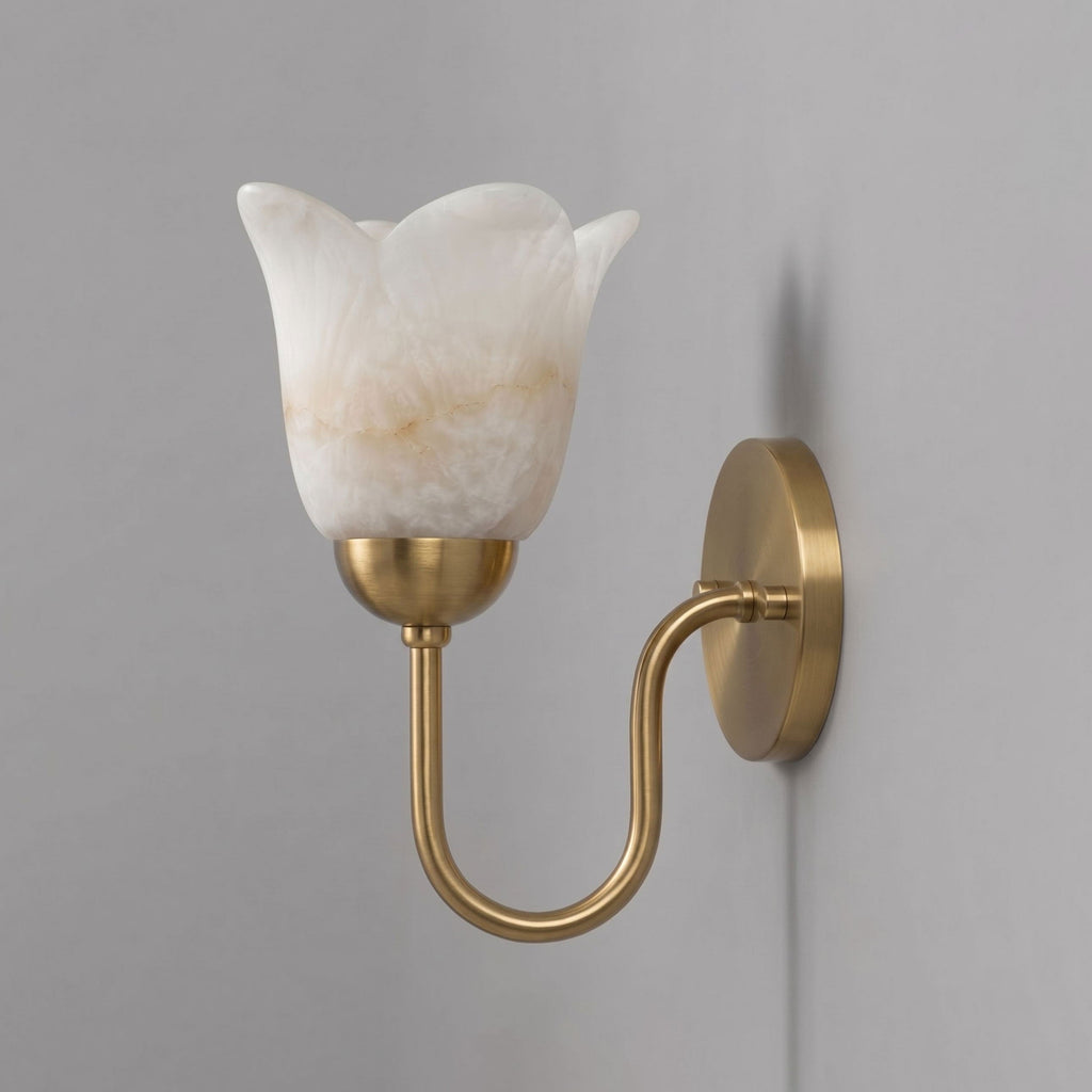 This brushed brass Clérachic wall sconce stands unlit on a plain grey wall, its S-curve arm and cord visible.