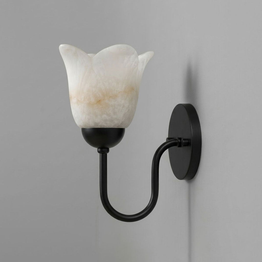 This matte black Clérachic wall sconce shows its petal-edged alabaster shade unlit against a plain grey wall.