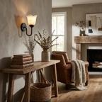 This matte black Clérachic wall sconce lights a living room corner beside a stone fireplace and a leather armchair.